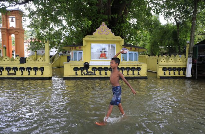 A boy with a packet of food wading through flood waters.